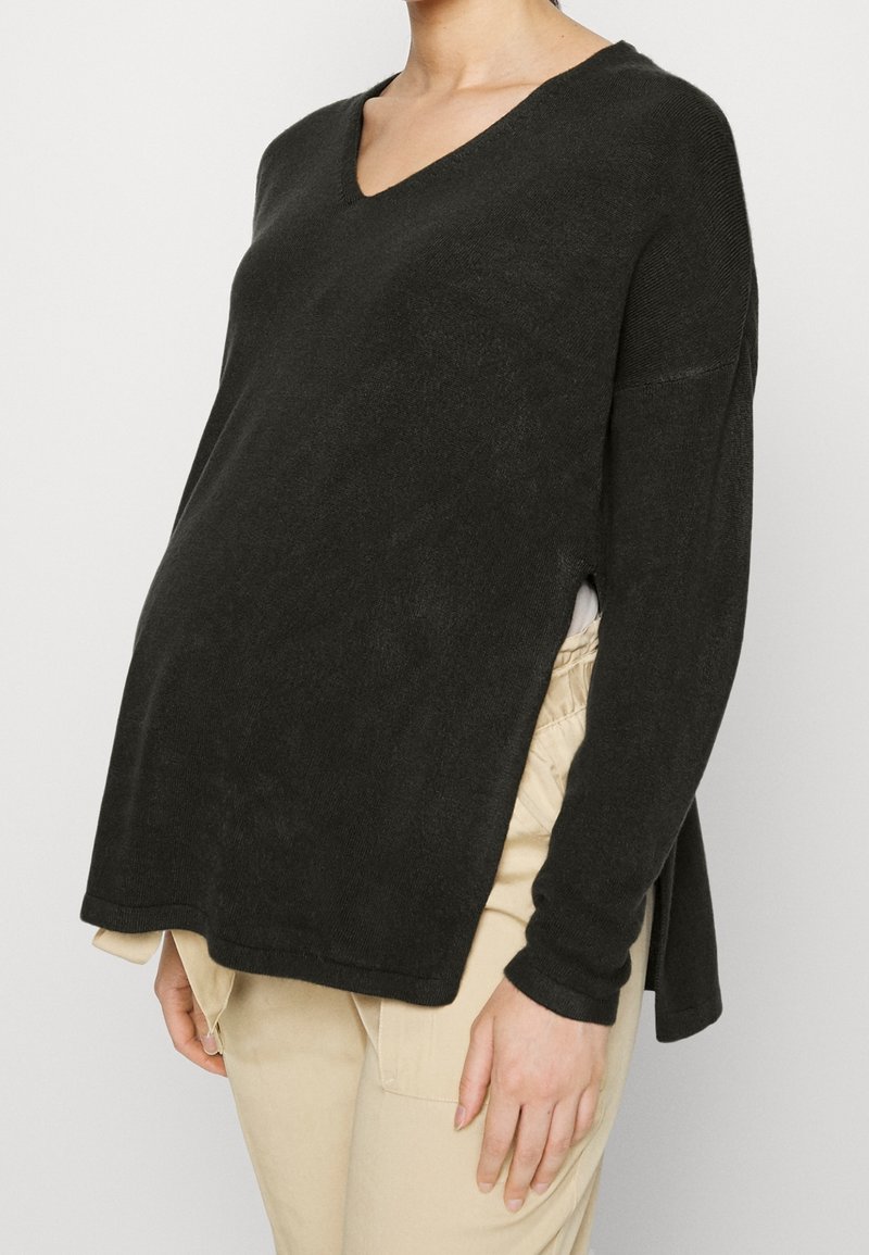 Svart v-ringad tröja i mjukt material, med långa ärmar, sidoklipp och en lös passform, i kombination med beige byxor.