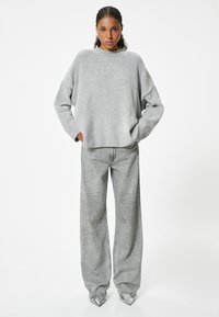 Grauer Strickpullover mit lockerer Passform und geripptem Ausschnitt, kombiniert mit weit geschnittenen, hellgrauen Jeans, die eine subtile Texturierung und eine entspannte Silhouette aufweisen.