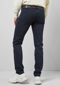 Navyblauwe katoenen broek met een slim fit, achterzakken en contrasterende stiksels. Gecombineerd met witte sportschoenen en een lichtgekleurde trui.
