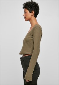 Olivgrünes, tailliertes Langarmoberteil mit tiefem V-Ausschnitt, aus weichem Material, kombiniert mit dunkelblauen, engen Jeans. Lässiges, modernes Design.