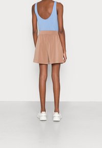 Débardeur sans manches bleu associé à un short beige à taille élastique, présentant une coupe décontractée. Le short a une texture lisse et un design simple.