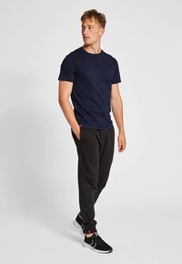 Mörkblå t-shirt med kort ärm kombinerad med svarta mjukisbyxor och svarta sportskor, med en slät textur och en figurnära design.