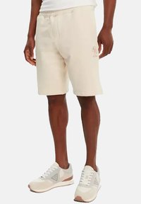 Beige katoenen sportshorts met een elastische tailleband, voorzien van zijzakken en een geborduurd logo op de voorkant.