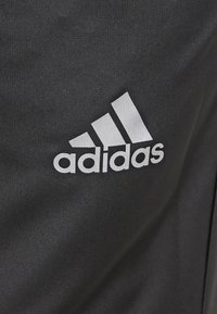 Černé sportovní oblečení s výrazným bílým logem Adidas a třemi diagonálními pruhy nad názvem značky napsaným malými písmeny.