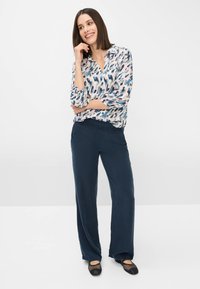 Blouse légère à motifs en bleu, rose et blanc ; associée à un pantalon ample navy ; ballerines noires ouvertes avec des détails en maille.