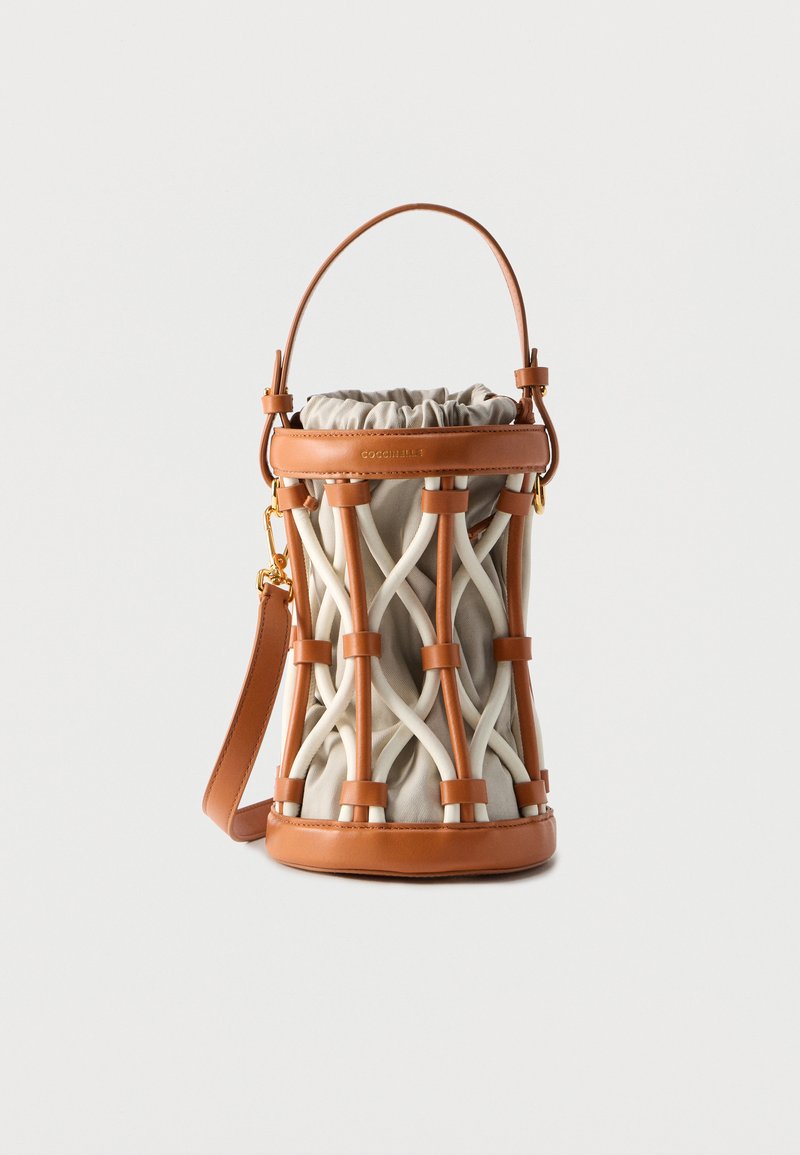 Μικρή κυλινδρική τσάντα από μπεζ ύφασμα, περικλειόμενη σε ένα διασταυρούμενο κλουβί από ταμπά δέρμα, με ταίριαστο δερμάτινο χερούλι και λουράκι.