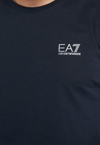 Námořnická modrá bavlněná tričko s kulatým výstřihem a malým vyšitým logem EA7 Emporio Armani na hrudi v stříbrné barvě.