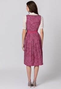 Pink paisley-patterned dress with a fitted bodice, pleated skirt, and a contrasting belt. Features a textured white lace overlay on sleeves.