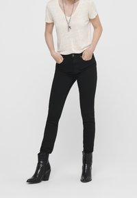 Svarta tajta jeans har hög midja, framfickor och knappstängning, i kombination med en ljusbeige V-ringad t-shirt och svarta ankelboots.