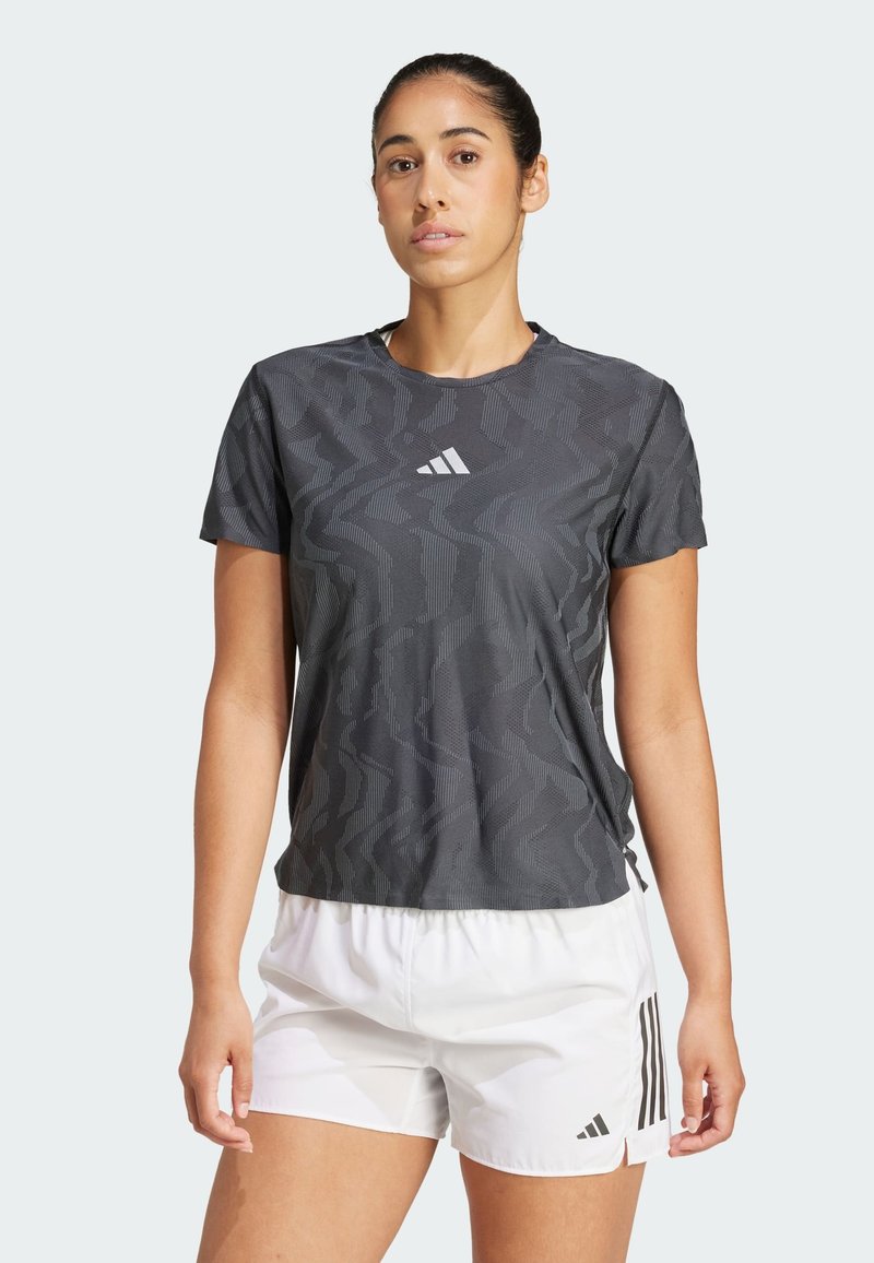 Maglietta atletica grigia con un sottile motivo ondulato, maniche corte, scollatura arrotondata e logo riflettente sul petto; abbinata a pantaloni corti bianchi.