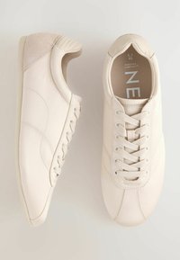 Light beige sneakers with a smooth synthetic upper, round toe, lace closure, and a soft suede accent on the heel.