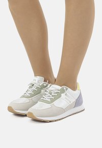 Zapatillas blancas y de colores pastel con material de malla, diseño de cordones y suela de goma. Presentan acentos en verde y lavanda en la parte superior.