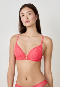 Soutien-gorge en dentelle corail avec un décolleté en V, doté de bretelles ajustables, de motifs floraux et d'un fermoir à l'avant.