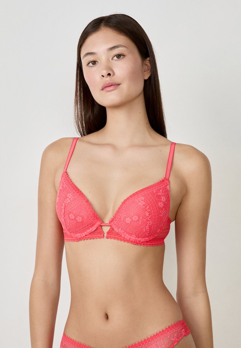 Soutien-gorge en dentelle corail avec un décolleté en V, doté de bretelles ajustables, de motifs floraux et d'un fermoir à l'avant.