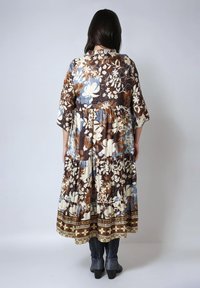 Femme aux longs cheveux noirs portant une robe midi florale marron, bleue et crème avec des manches à mi-longueur et des bottes à talons noires.