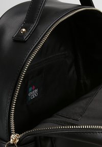 Czarna torebka z eko skóry z zamkiem w kolorze złotym, wyposażona w przestronne wnętrze oraz małą kieszonkę na zamek. Wewnątrz widoczna metka z logo marki.