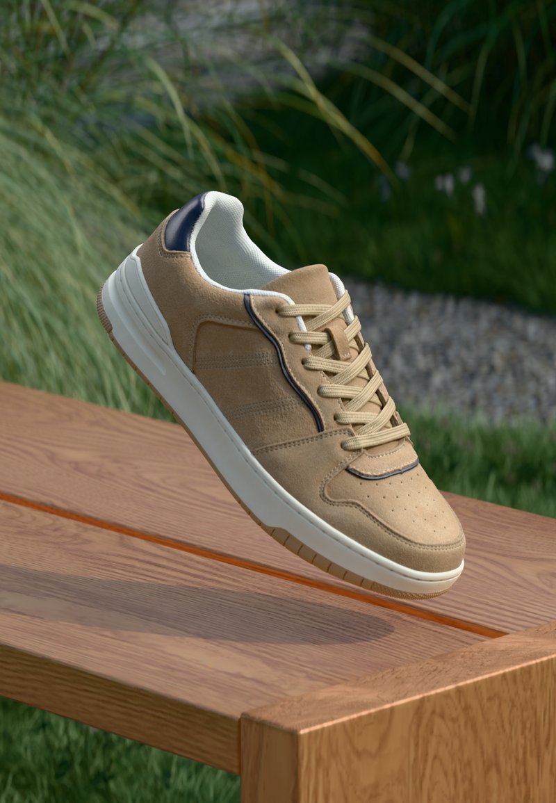 Μπεζ σουέτ αθλητικά παπούτσια με λευκή καουτσούκ σόλα, χαρακτηριστικά μπεζ κορδόνια, μπλε ναυτική λεπτομέρεια και τρυπητό σχέδιο στην περιοχή των δακτύλων.