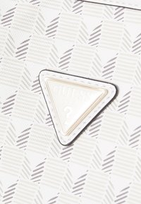 Valkoinen käsilaukku, jossa on teksturoitu pinnan kuvio geometrisillä muodoilla vaaleanharmaana ja tummanharmaana. Kultainen kolmiomainen logotunnus.