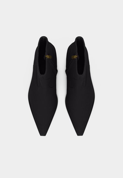 Pair of black pointed-toe ankle boots with gold zipper details viewed from above on a white background.