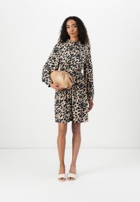 Leopardmønstret kjole i beige og sort, lange ballonærmer, indsnævret talje, parret med en beige clutch og lyse sandaler.
