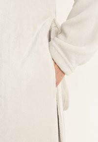 Ljusgrå fleecebadrock med en ficka och uppvikta ärmslut, tillverkad av ett mjukt, texturerat tyg och med en minimalistisk design.