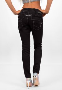 Zwarte jeans met een slim fit, witte stiksels, decoratieve achterzakken en een lichte glans, gecombineerd met iriserende hakken.