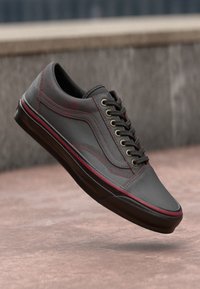 Baskets grises avec une tige en cuir lisse, œillets dorés, semelle noire et accents rouges. Caractéristiques d'un bout arrondi et d'un design classique à laçage.