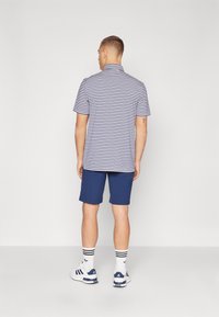 Polo w paski z kołnierzykiem w granatowym i białym kolorze, zestawiony z jednolitymi, niebieskimi szortami. Model nosi białe trampki z granatowymi akcentami oraz w paski skarpetki.