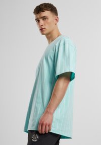 T-shirt surdimensionné vert menthe avec des rayures verticales blanches, manches courtes et col rond. Agrémenté d'un patch logo circulaire sur la manche.
