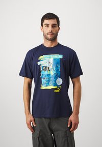 Jūras zilas kokvilnas T-krekls ar krāsainu grafisko dizainu, kurā ir teksts un logotips. Apaļš kakla izgriezums un īsas piedurknes.