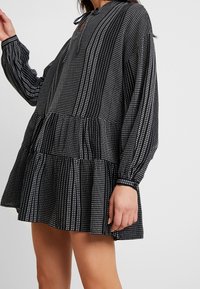 Vestido negro y blanco con estampado, de manga larga, diseño de peplum, con cuello en forma de llave abotonado y tela texturizada.