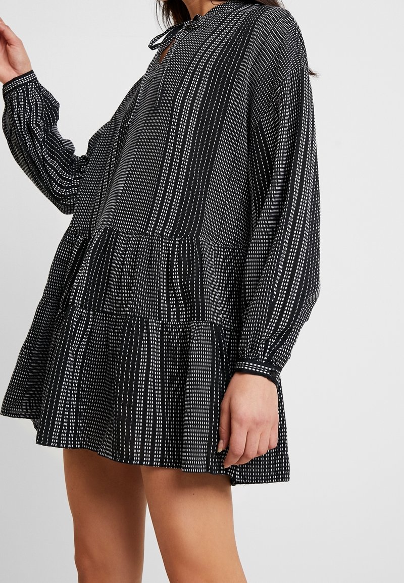 Vestido negro y blanco con estampado, de manga larga, diseño de peplum, con cuello en forma de llave abotonado y tela texturizada.