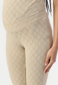 Beige leggings med et teksturert diamantmønster, høy midje og glattere finish, som viser en nærbilde av stoffet og detaljene.