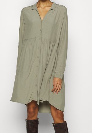Light olive long-sleeve button-up shirt dress with gathered waist, worn with dark brown knee-high boots on standing person.