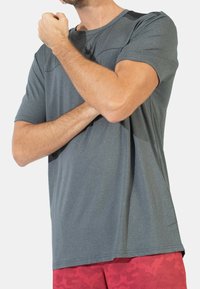 Grijze sportt-shirt met korte mouwen en een ronde hals, voorzien van een klein spinnenlogo op de borst en subtiele accentdetails op de schouders.