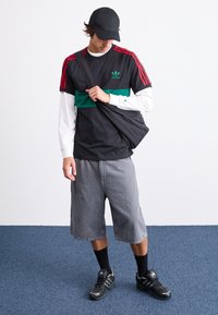 Svart t-shirt med röda detaljer och grön rand, grå shorts, svart keps, svarta sneakers och svarta strumpor. Avslappnad atletisk outfit.