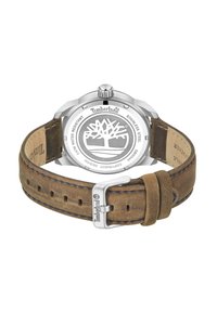 Timberland laikrodis su nerūdijančio plieno korpusu, rudos odos dirželiu, mėlynu siūlu ir graviruotu logotipu korpuso gale, kuriame pavaizduota medžio dizainas.
