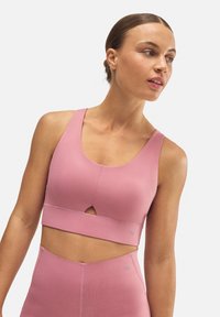 Sujeción deportiva rosa hecha de un material suave y elástico, con un escote redondeado, detalle recortado y un sutil acento de logo cerca del dobladillo.