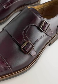 Bordeaux leren schoenen met twee metalen gespen, een gladde textuur, ronde neus, stiksels en een contrasterende lichte zool.