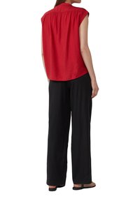 Chemise rouge à manches courtes avec un dos froncé et une coupe décontractée, associée à un pantalon large noir et des sandales plates. Texture de tissu lisse.