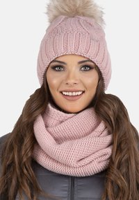 Berretto lavorato a maglia rosa con pom-pom in pelliccia e design a coste; abbinato a una sciarpa infinita lavorata a maglia rosa, entrambi con una texture morbida.