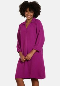 Robe violette avec un col, des manches longues bouffantes et une coupe décontractée. Fabriquée à partir d'un tissu texturé, longueur genou avec une finition lisse.