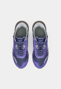 Pāris purpura un jūras zilas Reebok kedas ar šņorēm, skatoties no augšas uz balta fona.