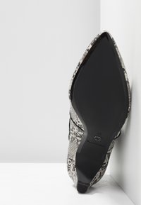 Chaussure à talon haut à bout pointu arborant un motif serpent noir et blanc texturé, avec une semelle noire brillante et des détails de couture subtils.