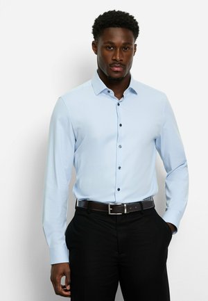 Light blue long-sleeve shirt with a button-down collar, featuring dark buttons and a textured fabric, worn with black trousers and a brown belt.