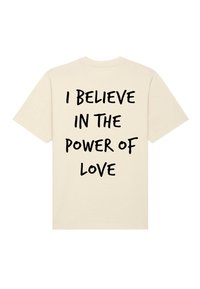 Crème-kleurig T-shirt met vetgedrukte, zwarte tekst op de achterkant die luidt: "IK Geloof IN DE KRAACHT VAN LIEFDE." Zachte katoenen stof, korte mouwen.