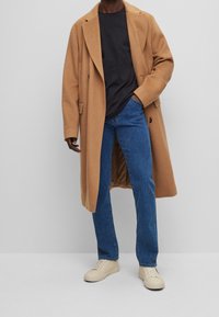 Abrigo de mezcla de lana color camello con solapas estructuradas, camiseta negra, jeans azules y zapatillas beige. Diseño sencillo y estilizado en colores neutros.