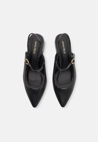 Black pointed-toe slingback shoes with a low heel, featuring a shiny leather finish and a gold-toned buckle accent on the strap.