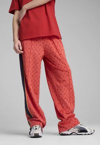 Rode sweatpants met patroon en losse pasvorm, voorzien van plooien, zijzakken en contrasterende donkerblauwe en gele strepen aan de zijkanten.