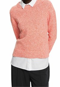 Neulottu villapaita korallin sävyssä, jossa on pyöreä pääntie ja teksturoitu, hieman väljä istuvuus. Päällä valkoinen kauluspaita.